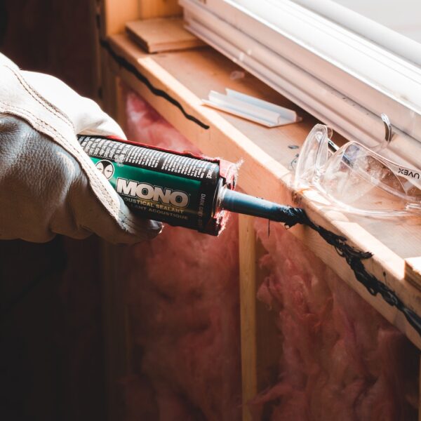 Crop unrecognizable workman in glove applying caulk from bottle on seam during window montage work in building
