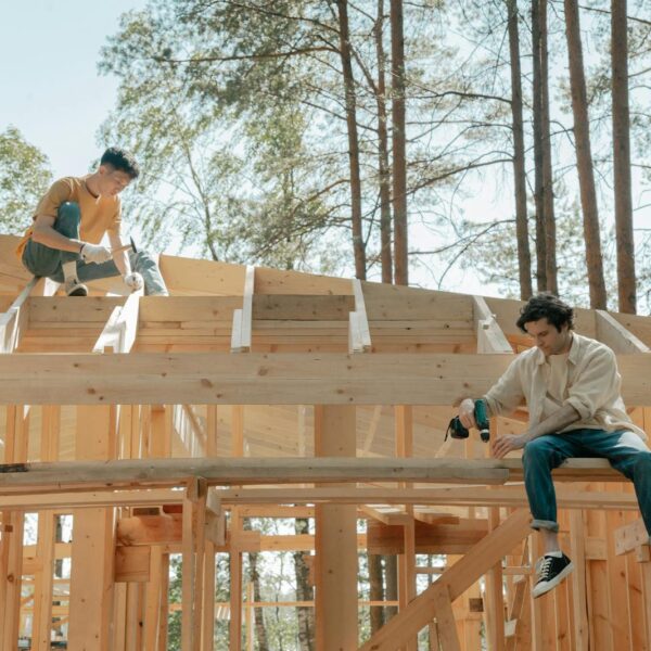 Two male carpenters working on a wooden framework of a house under bright daylight.