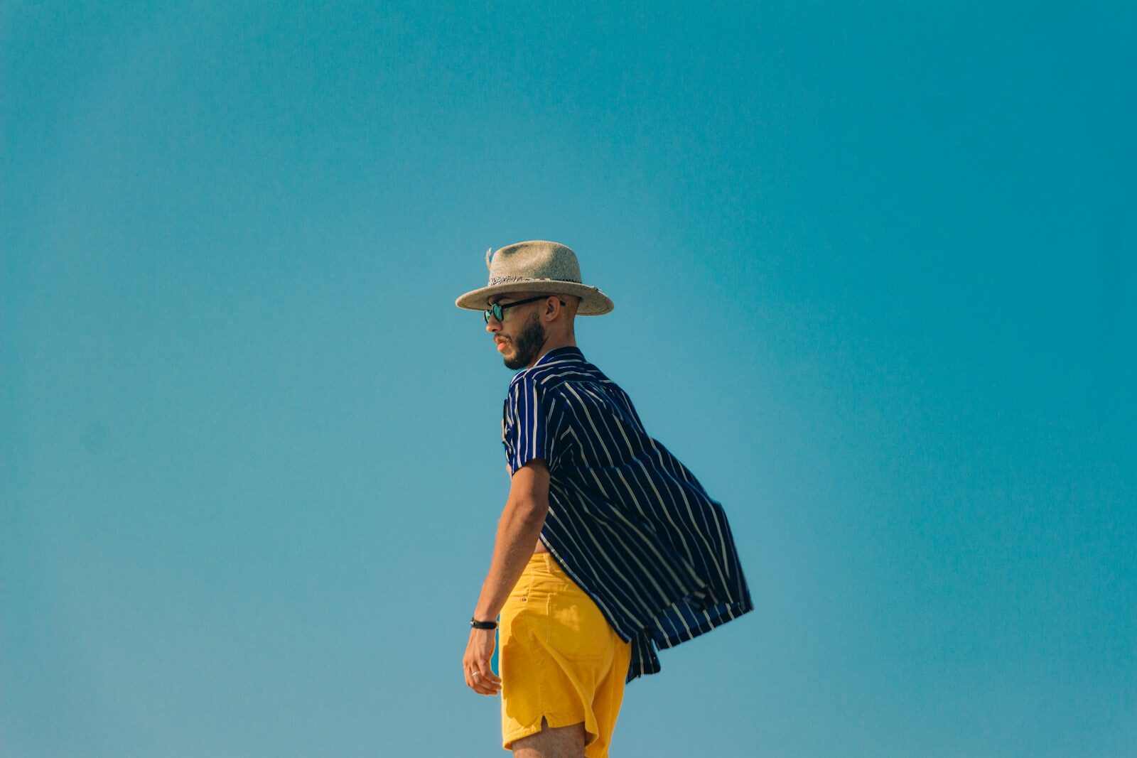 Man in stylish summer outfit posing under blue sky.
